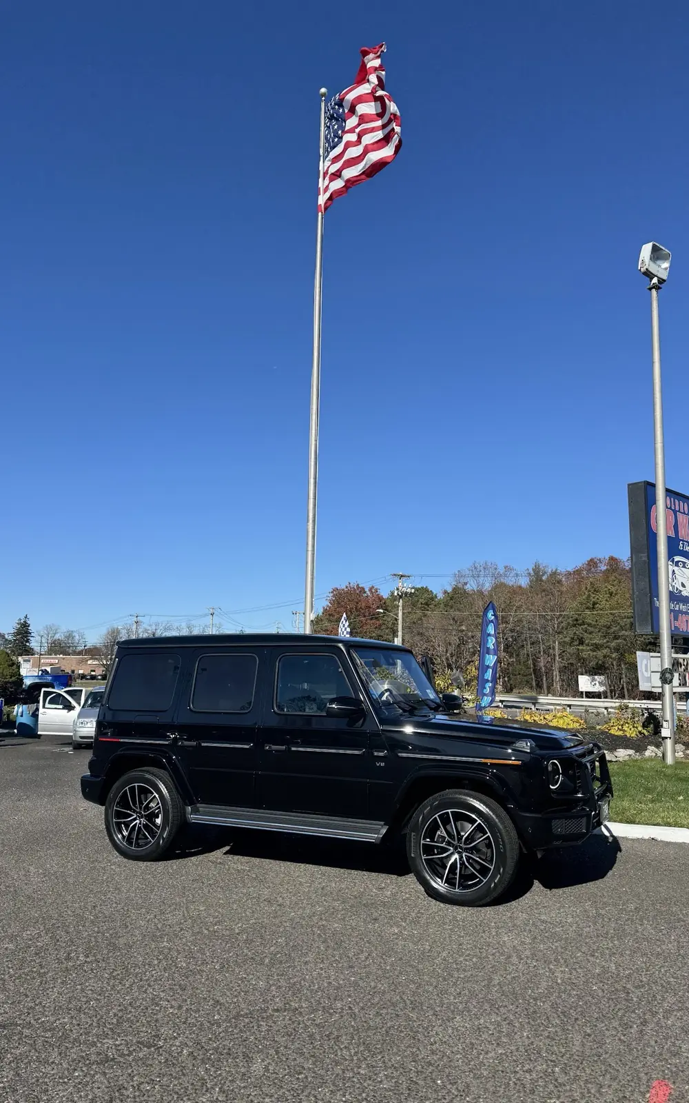 A black Mercedes G-Wagon parked under the American flag on the wash lot